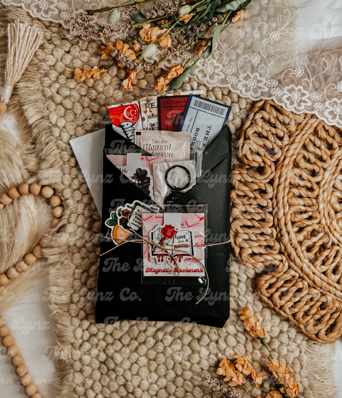 Blind Date With a Book package wrapped in black paper, tied with twine, and filled with bookish extras including a magnetic bookmark, stickers, candy, and themed inserts on a cozy boho background with florals and textured rugs.